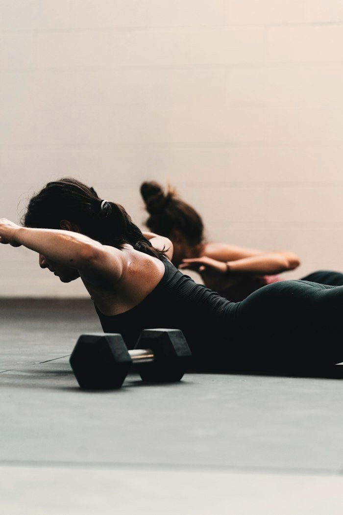 Two women doing a floor exercise next to dumbbells